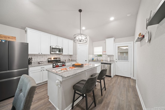 kitchen featuring appliances with stainless steel finishes, a center island, white cabinetry, light stone counters, and hardwood / wood-style flooring