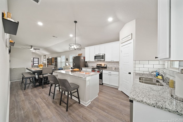 kitchen featuring stainless steel appliances, sink, a center island, vaulted ceiling, and white cabinets