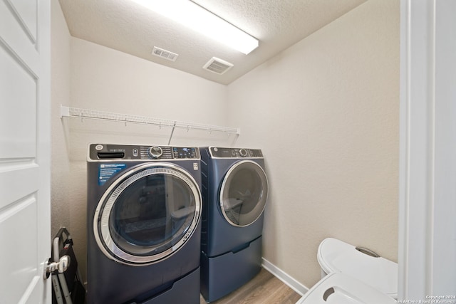 washroom with a textured ceiling, washer and dryer, and wood-type flooring