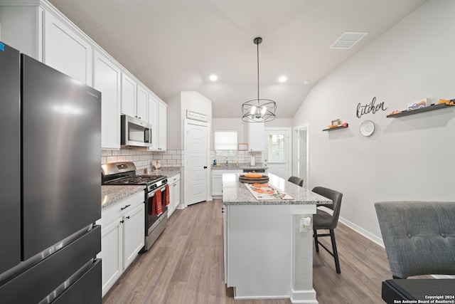 kitchen with white cabinetry, light hardwood / wood-style floors, stainless steel appliances, pendant lighting, and a breakfast bar area