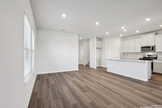 kitchen featuring appliances with stainless steel finishes, light hardwood / wood-style floors, white cabinetry, and a kitchen island with sink