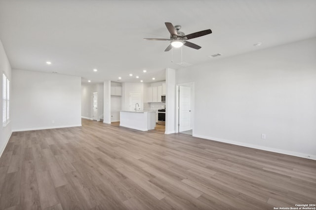 unfurnished living room with light wood-type flooring, ceiling fan, and sink