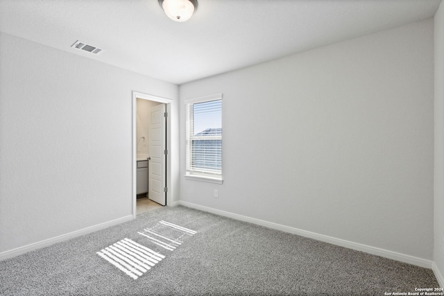 unfurnished bedroom with ensuite bathroom and light carpet