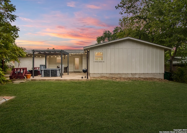 back house at dusk with a pergola, a patio, and a yard