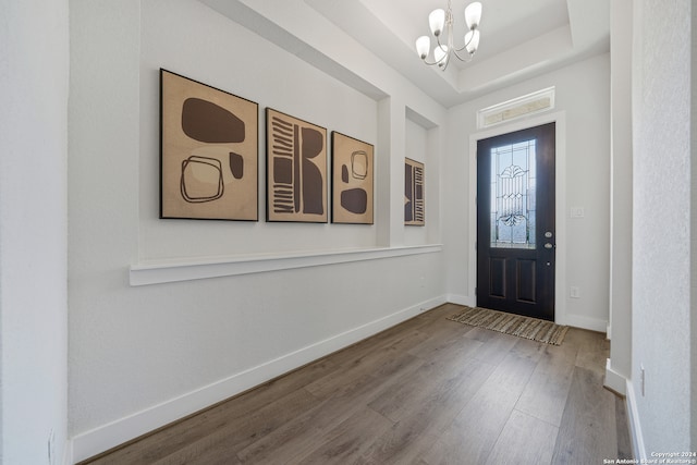 entryway with a notable chandelier, hardwood / wood-style flooring, and a raised ceiling