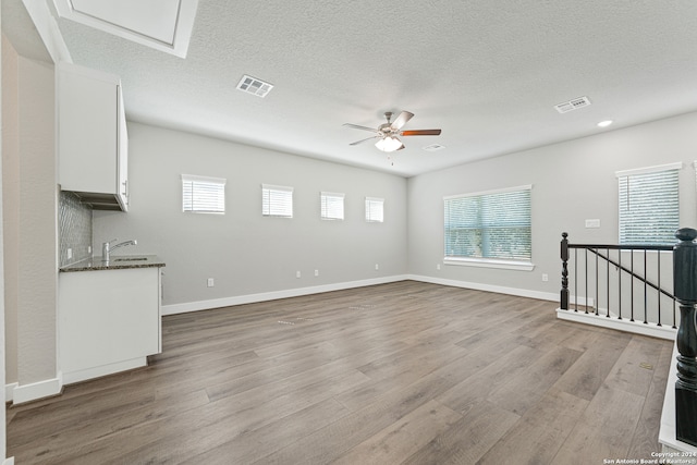 unfurnished living room featuring light hardwood / wood-style floors, a textured ceiling, sink, and ceiling fan