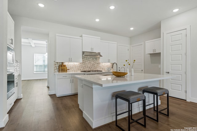 kitchen with beamed ceiling, stainless steel appliances, a center island with sink, white cabinets, and dark hardwood / wood-style flooring