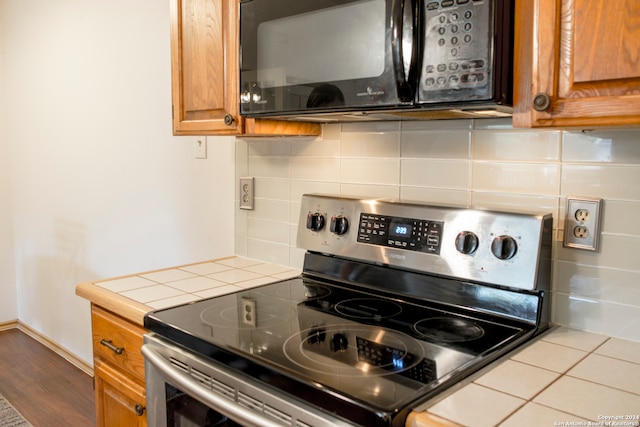 kitchen featuring decorative backsplash, stainless steel electric stove, tile counters, and wood-type flooring