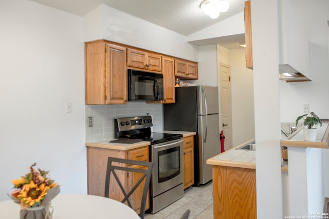 kitchen featuring tasteful backsplash, light tile patterned flooring, a textured ceiling, stainless steel appliances, and lofted ceiling