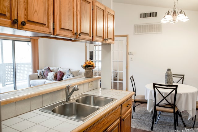 kitchen with hanging light fixtures, tile countertops, a chandelier, vaulted ceiling, and sink