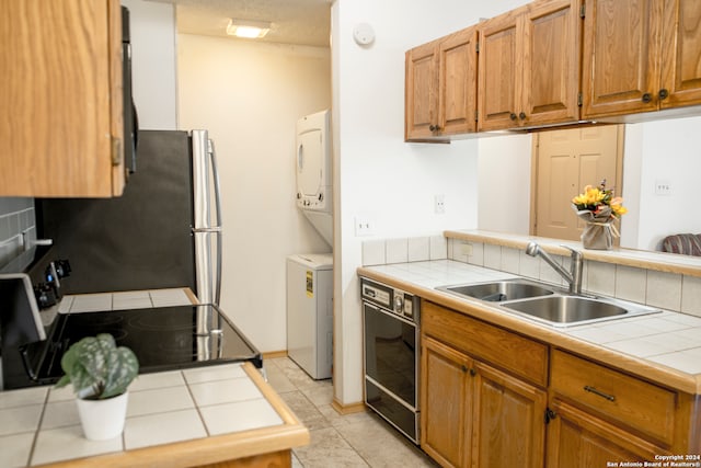 kitchen with light tile patterned floors, stacked washer and dryer, electric stove, tile counters, and sink