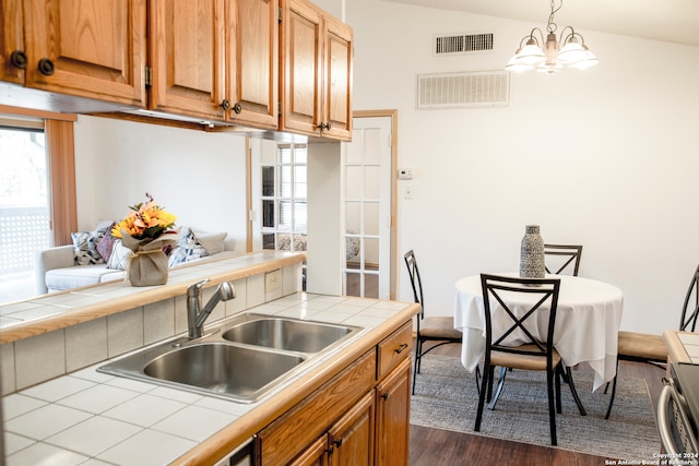 kitchen with lofted ceiling, dark hardwood / wood-style floors, tile countertops, sink, and a notable chandelier