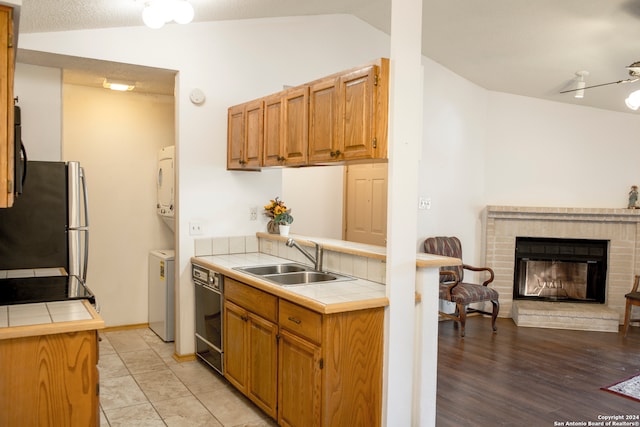 kitchen featuring lofted ceiling, stainless steel fridge, light hardwood / wood-style flooring, tile counters, and sink