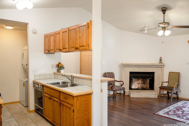 kitchen with tile counters, light hardwood / wood-style flooring, sink, vaulted ceiling, and a fireplace