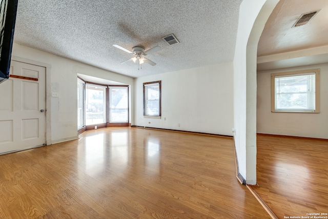 unfurnished room featuring a textured ceiling, ceiling fan, light wood-type flooring, and a wealth of natural light