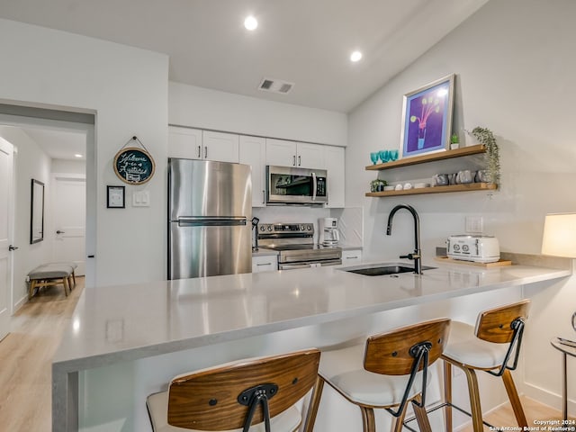 kitchen with kitchen peninsula, appliances with stainless steel finishes, white cabinetry, light hardwood / wood-style flooring, and sink