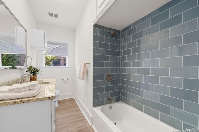 full bathroom with toilet, tiled shower / bath, hardwood / wood-style flooring, and vanity