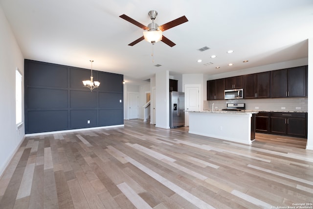 kitchen featuring tasteful backsplash, light stone counters, appliances with stainless steel finishes, light hardwood / wood-style floors, and decorative light fixtures