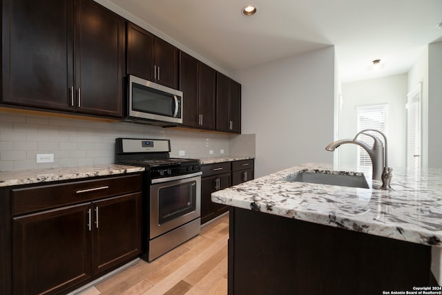 kitchen featuring tasteful backsplash, sink, light wood-type flooring, dark brown cabinets, and stainless steel appliances