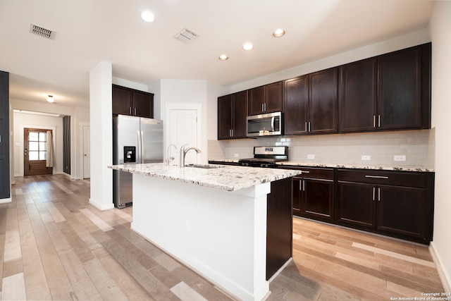 kitchen featuring appliances with stainless steel finishes, sink, light wood-type flooring, and a center island with sink