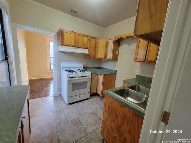 kitchen with a sink, dark countertops, white range with gas stovetop, under cabinet range hood, and ornamental molding