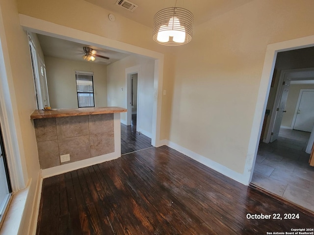 interior space with dark wood-type flooring, visible vents, baseboards, and ceiling fan with notable chandelier