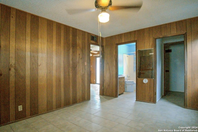 empty room with ceiling fan, a textured ceiling, and wooden walls