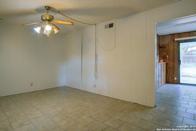 spare room featuring wood walls, a textured ceiling, and ceiling fan