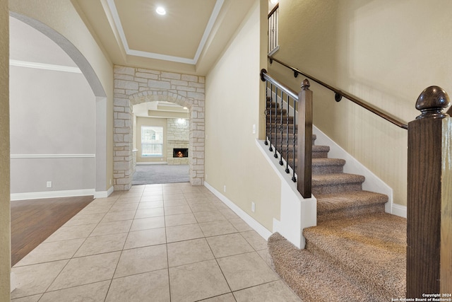 entrance foyer featuring crown molding, a stone fireplace, and light tile patterned floors