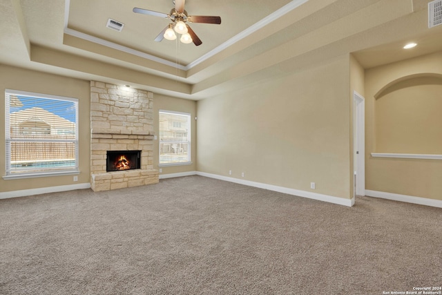 unfurnished living room featuring a tray ceiling, carpet flooring, a wealth of natural light, and a stone fireplace