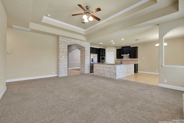 unfurnished living room with light carpet, ornamental molding, ceiling fan, and a raised ceiling