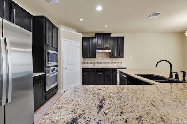 kitchen with light stone countertops, light tile patterned flooring, appliances with stainless steel finishes, sink, and decorative backsplash