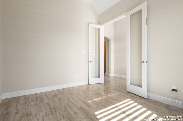 empty room with french doors, lofted ceiling, and light wood-type flooring