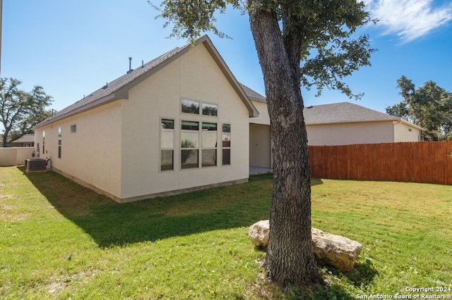 rear view of property with central AC unit and a lawn