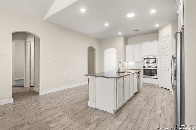 kitchen featuring white cabinetry, stainless steel appliances, dark stone counters, and an island with sink