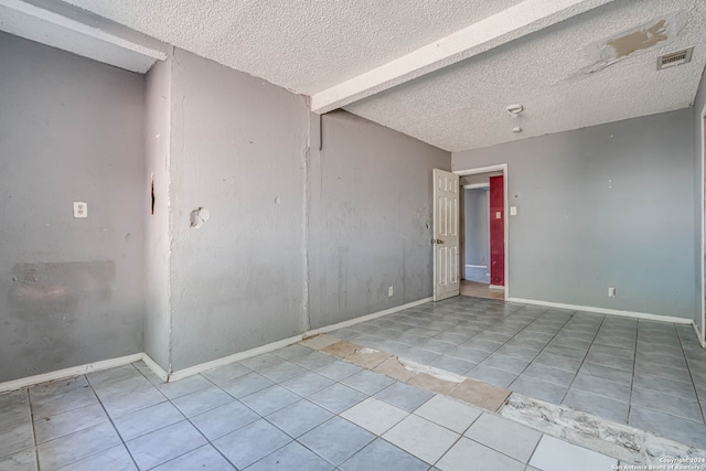 tiled empty room featuring a textured ceiling and beamed ceiling