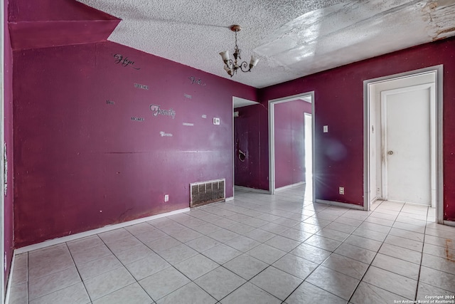 spare room featuring a notable chandelier, a textured ceiling, and light tile patterned floors