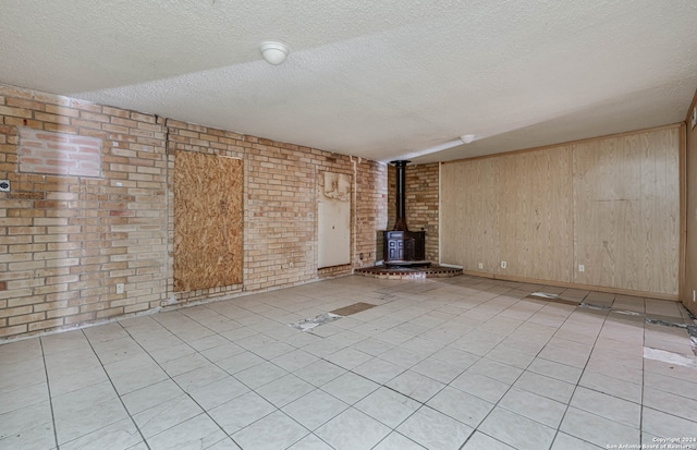 unfurnished living room featuring a wood stove, brick wall, light tile patterned flooring, a textured ceiling, and wood walls