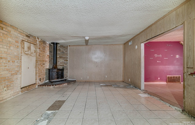 unfurnished living room with light tile patterned floors, a textured ceiling, a wood stove, and wood walls