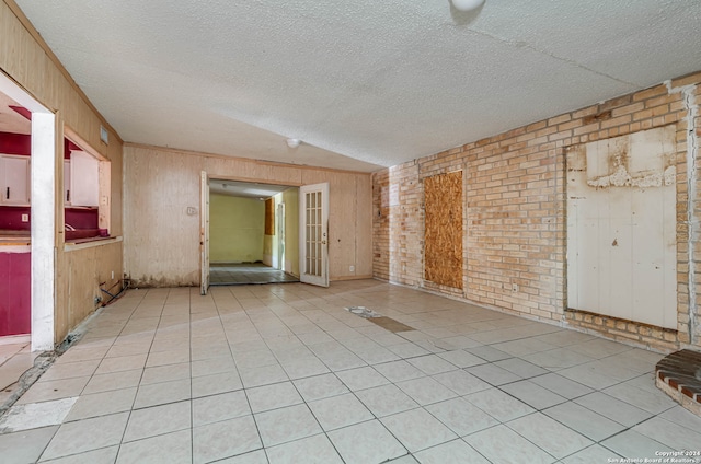 empty room with light tile patterned flooring, a textured ceiling, wooden walls, and brick wall