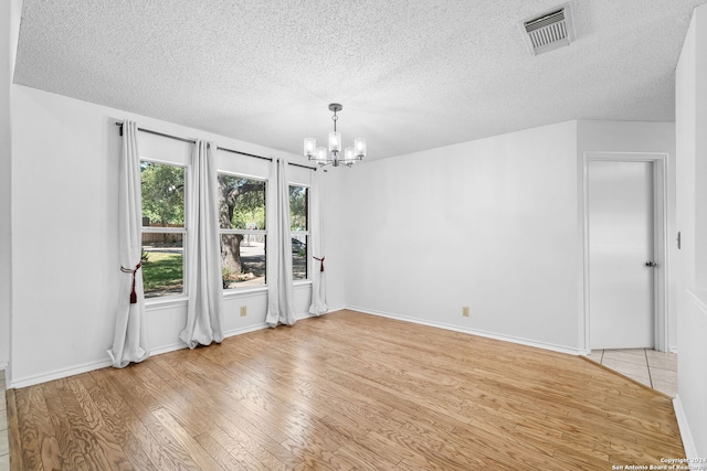 empty room featuring light wood-type flooring, a textured ceiling, and a notable chandelier