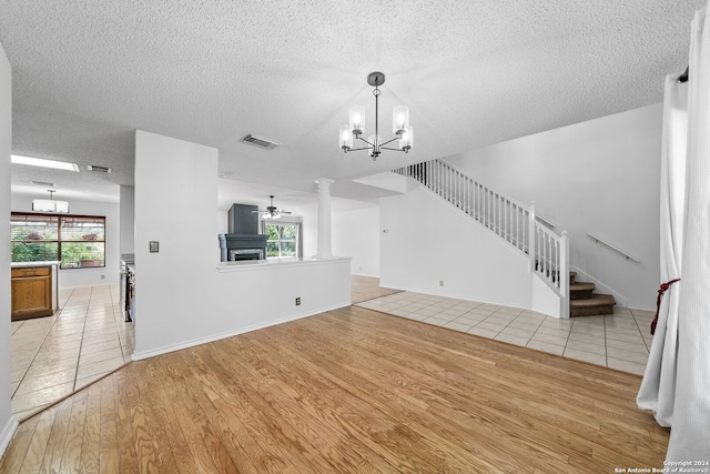 unfurnished living room featuring ceiling fan with notable chandelier, plenty of natural light, a textured ceiling, and light hardwood / wood-style flooring