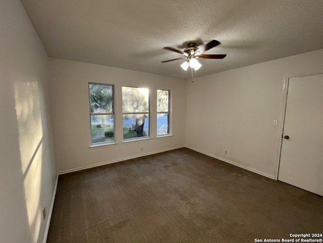 empty room featuring a textured ceiling, dark colored carpet, and ceiling fan