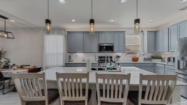 kitchen featuring appliances with stainless steel finishes, a kitchen island with sink, sink, and hanging light fixtures