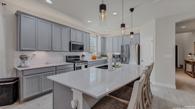 kitchen with appliances with stainless steel finishes, sink, a center island with sink, and hanging light fixtures