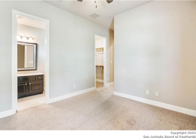 unfurnished bedroom with ceiling fan, a walk in closet, light colored carpet, and ensuite bath