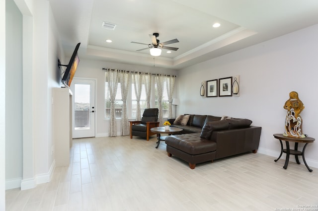 living room with a raised ceiling, light hardwood / wood-style floors, and ceiling fan