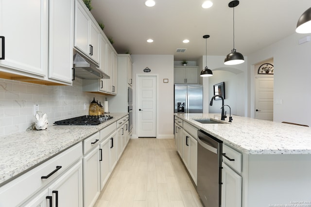 kitchen with an island with sink, light stone countertops, white cabinets, pendant lighting, and appliances with stainless steel finishes