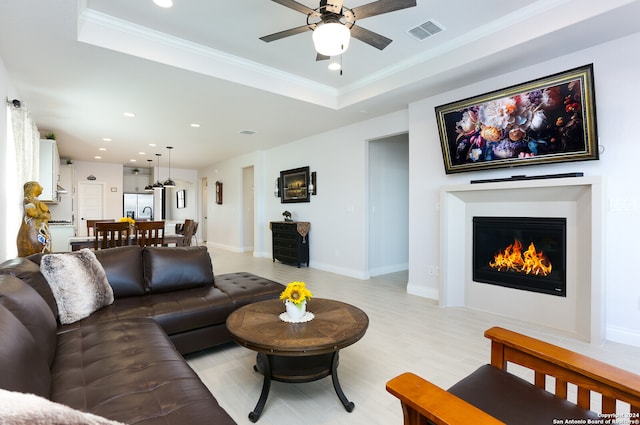 living room with light hardwood / wood-style flooring, crown molding, a tray ceiling, and ceiling fan