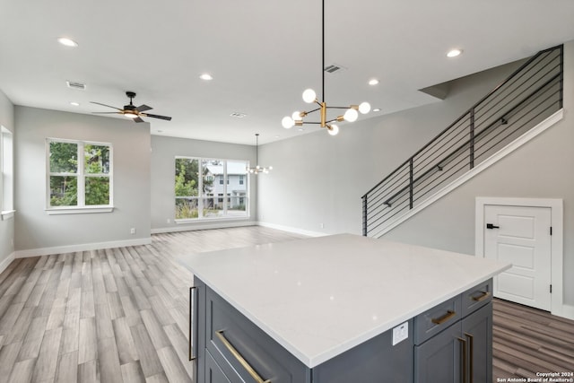 kitchen with wood-type flooring, ceiling fan with notable chandelier, a center island, hanging light fixtures, and gray cabinets